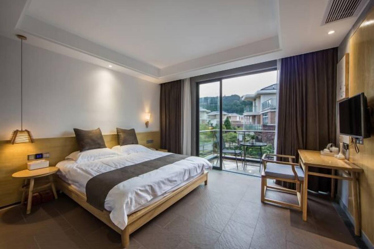 Habitación de hotel con una cama grande, un escritorio, una silla, un televisor y un balcón con vistas a edificios.
