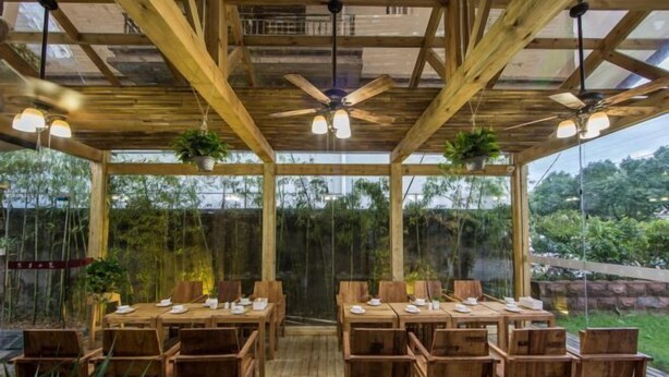 An outdoor wooden dining area with tables and chairs, ceiling fans, and hanging plants. - Yueming Xiaoyuan Hostel (Wuyishan)