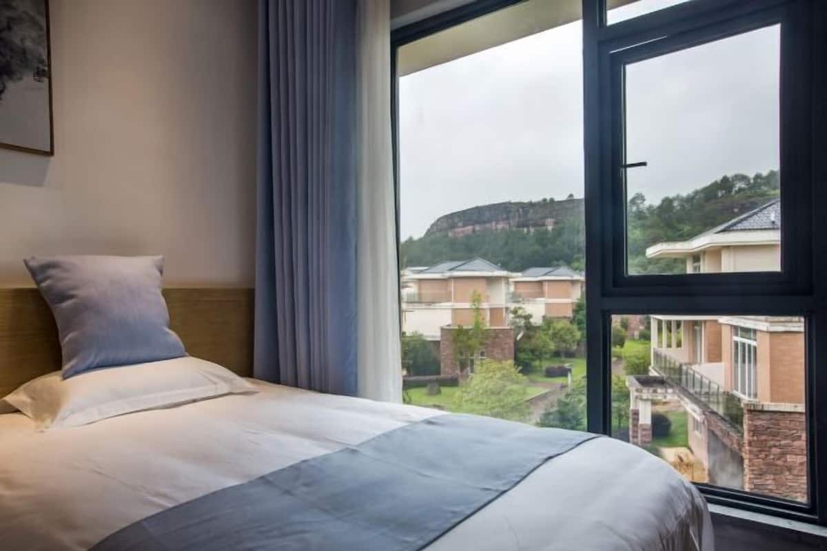 Una habitación de hotel con una cama grande, vistas a un complejo de edificios y una ventana con cortinas.