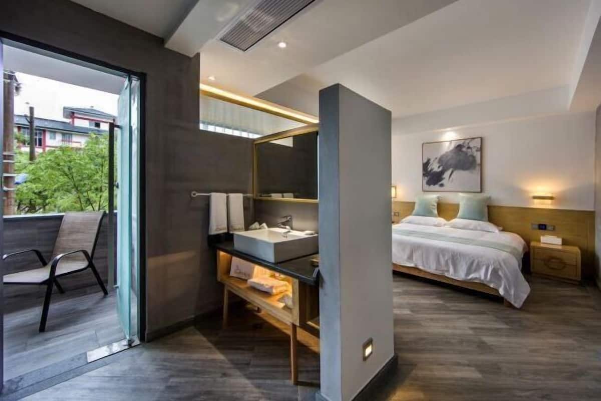Habitación de hotel moderna con un ventanal grande, un escritorio con lavamanos, una cama con cabecero y una mesita de noche con lámpara.