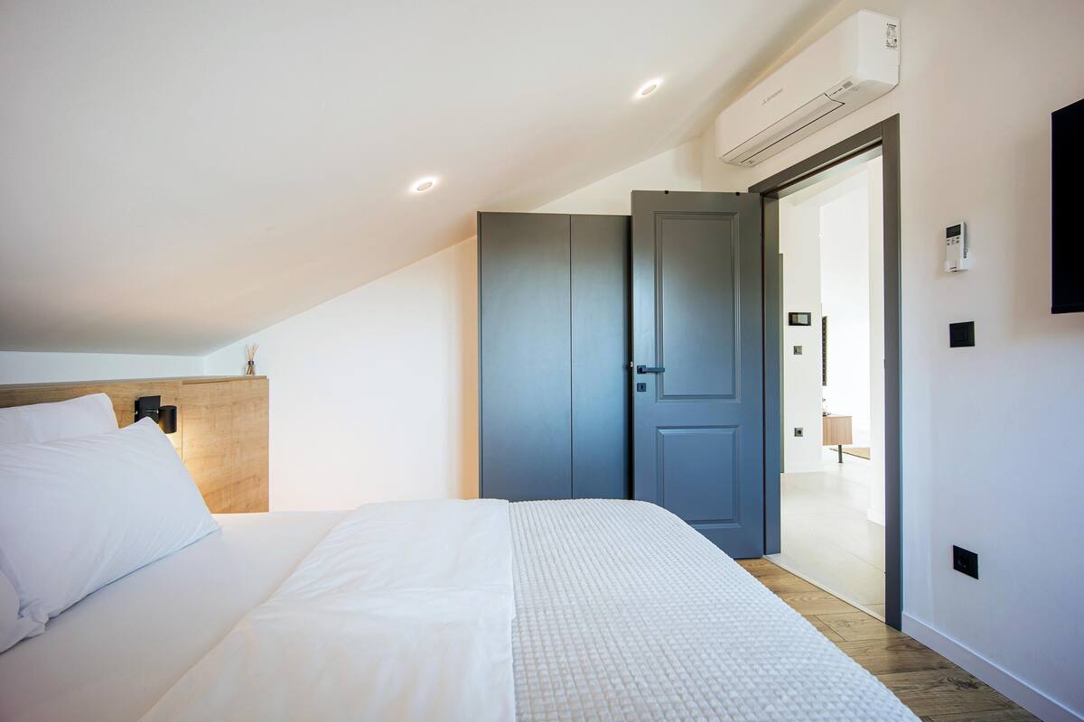 Un dormitorio moderno con una cama grande, cabecera de madera, un armario gris y un equipo de aire acondicionado.