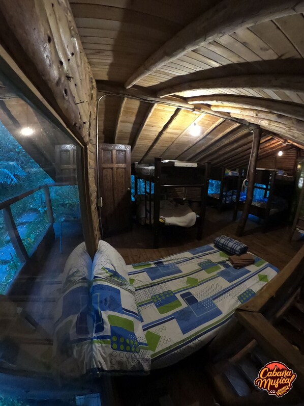 Una cabaña rústica con interior de madera, una cama con colcha y vistas al bosque a través de una ventana.