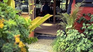 A rustic outdoor seating area with a wooden deck, surrounded by lush greenery and potted plants. - La Cabaña Musical (Medellín)