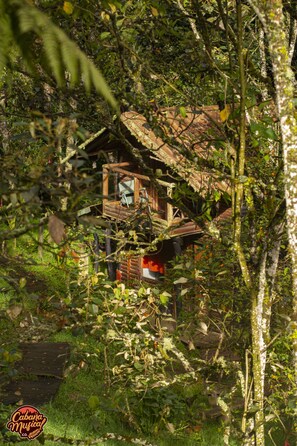 A rustic wooden cabin with a balcony, surrounded by dense foliage. - La Cabaña Musical (Medellín)