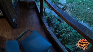 A wooden deck with a railing, a bench, and a view of a lush garden. - La Cabaña Musical (Medellín)