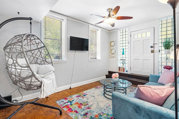 A living room with a hanging chair, a sofa, a coffee table, and a ceiling fan.
