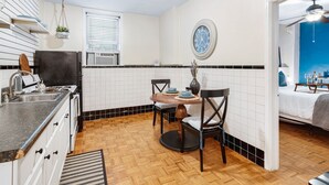 Una cocina compacta con paredes de azulejos blancos, suelo de madera y una zona de comedor con dos sillas y una mesa.