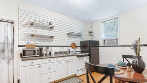 Una cocina moderna con armarios blancos, un refrigerador negro, un microondas y una estufa. Hay una mesa de comedor con sillas y un florero con flores.