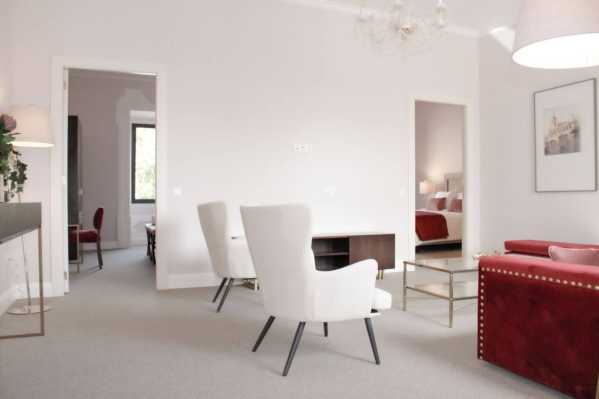 A modern living room with white furniture, a red sofa, and a chandelier.