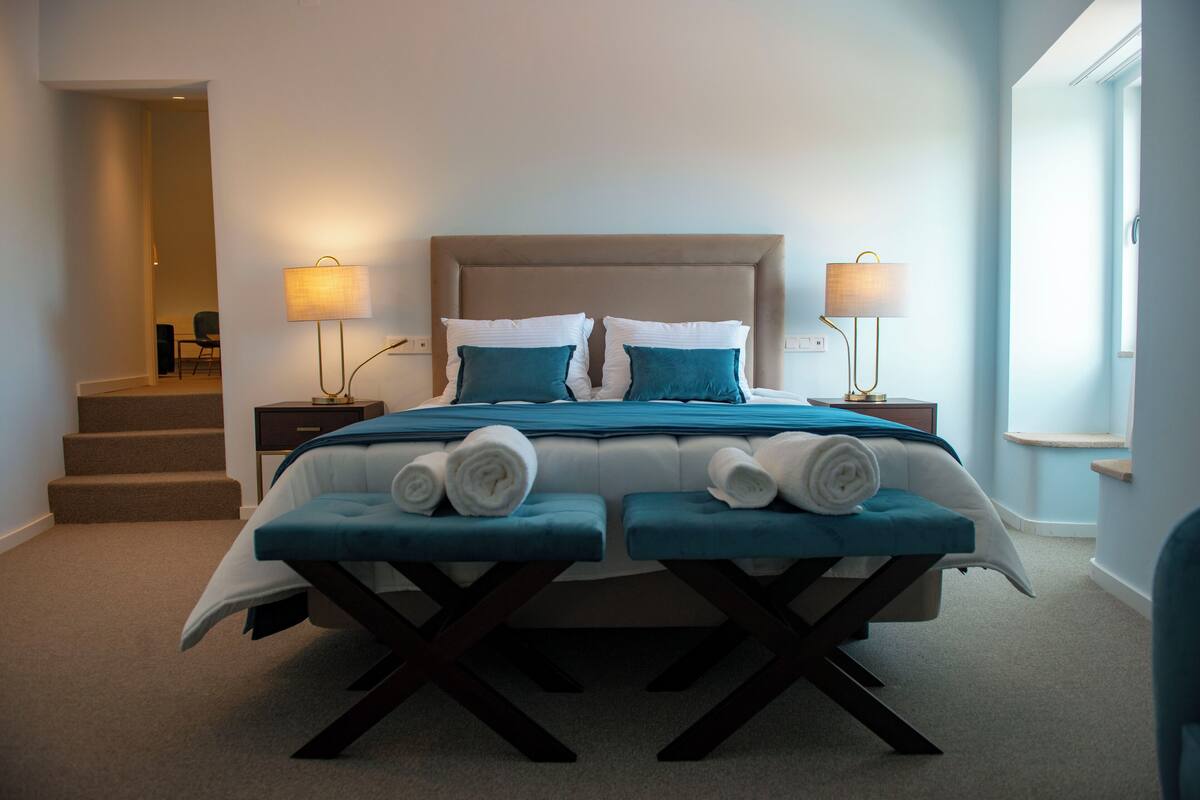 A bedroom with a bed, two bedside tables, a window, and a staircase.