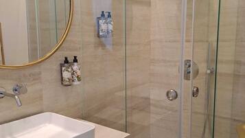 A modern bathroom with a glass-enclosed shower, a white sink, and a mirror with a gold frame.