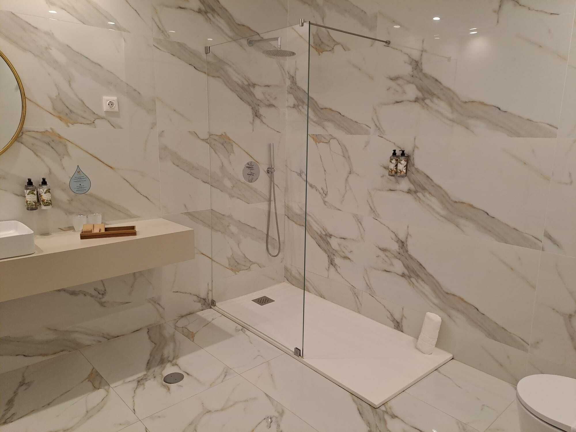 A modern bathroom with a marble floor and walls, a glass-enclosed shower, a white sink, and two hand soap dispensers.