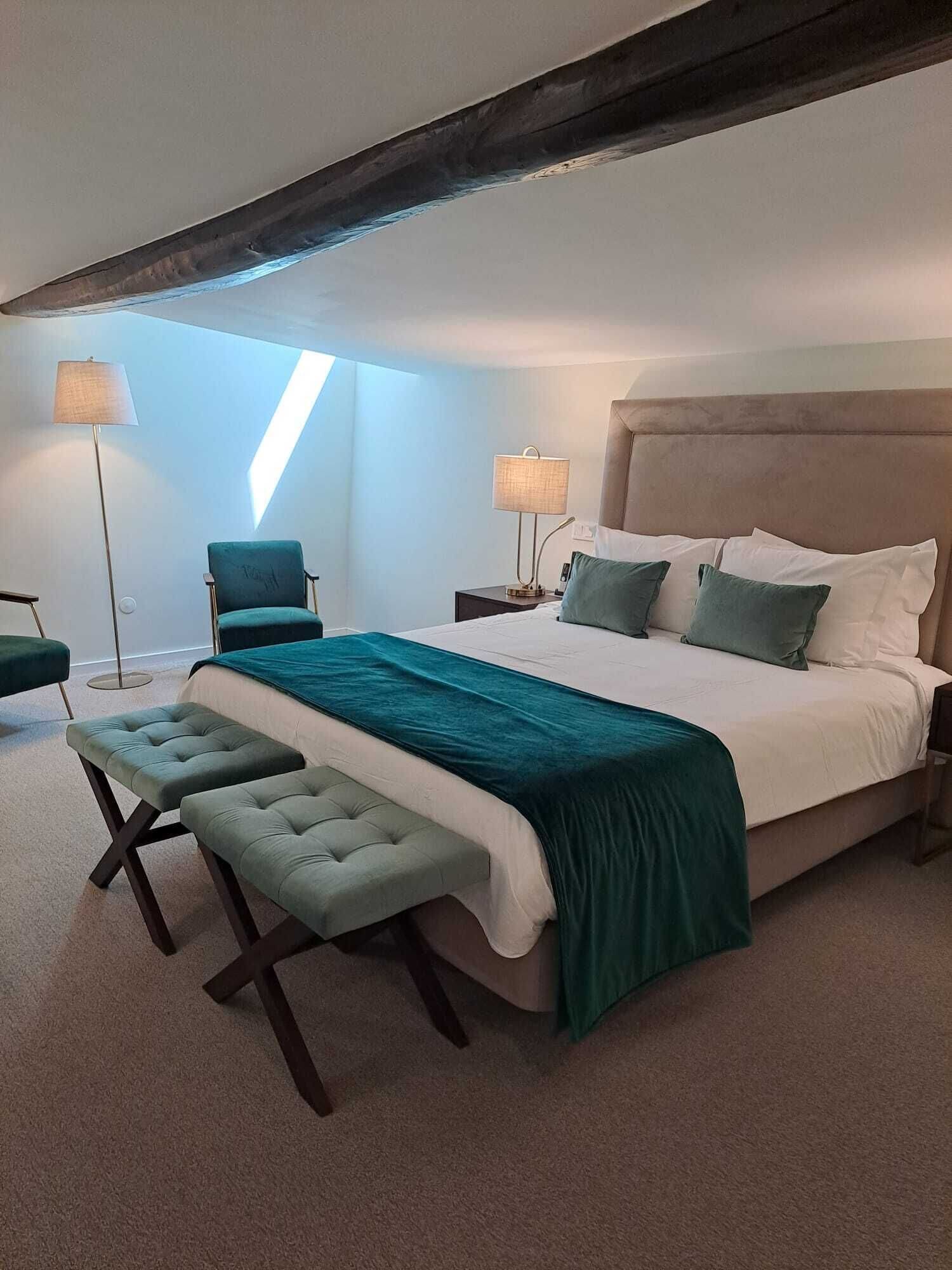 A bedroom with a large bed, two bedside tables, a chair, a bench, and a floor lamp.