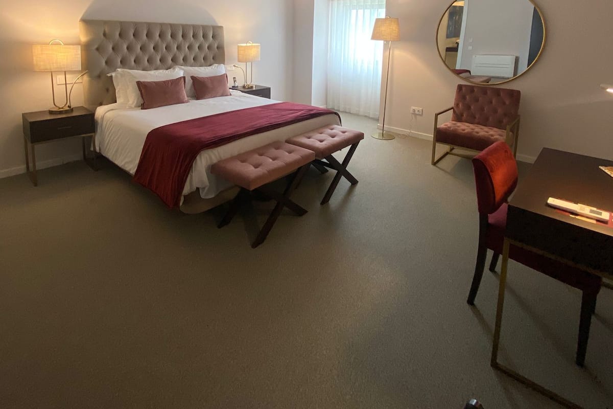 A hotel room with a large bed, bedside tables, a round mirror, a chair, and a desk.