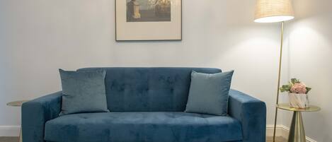 A blue sofa with gold studs, a framed picture on the wall, and a floor lamp with a gold base.