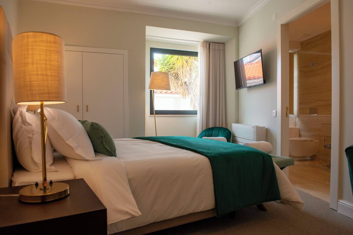 A hotel room with a bed, a bedside lamp, a television, and a view of the outside.