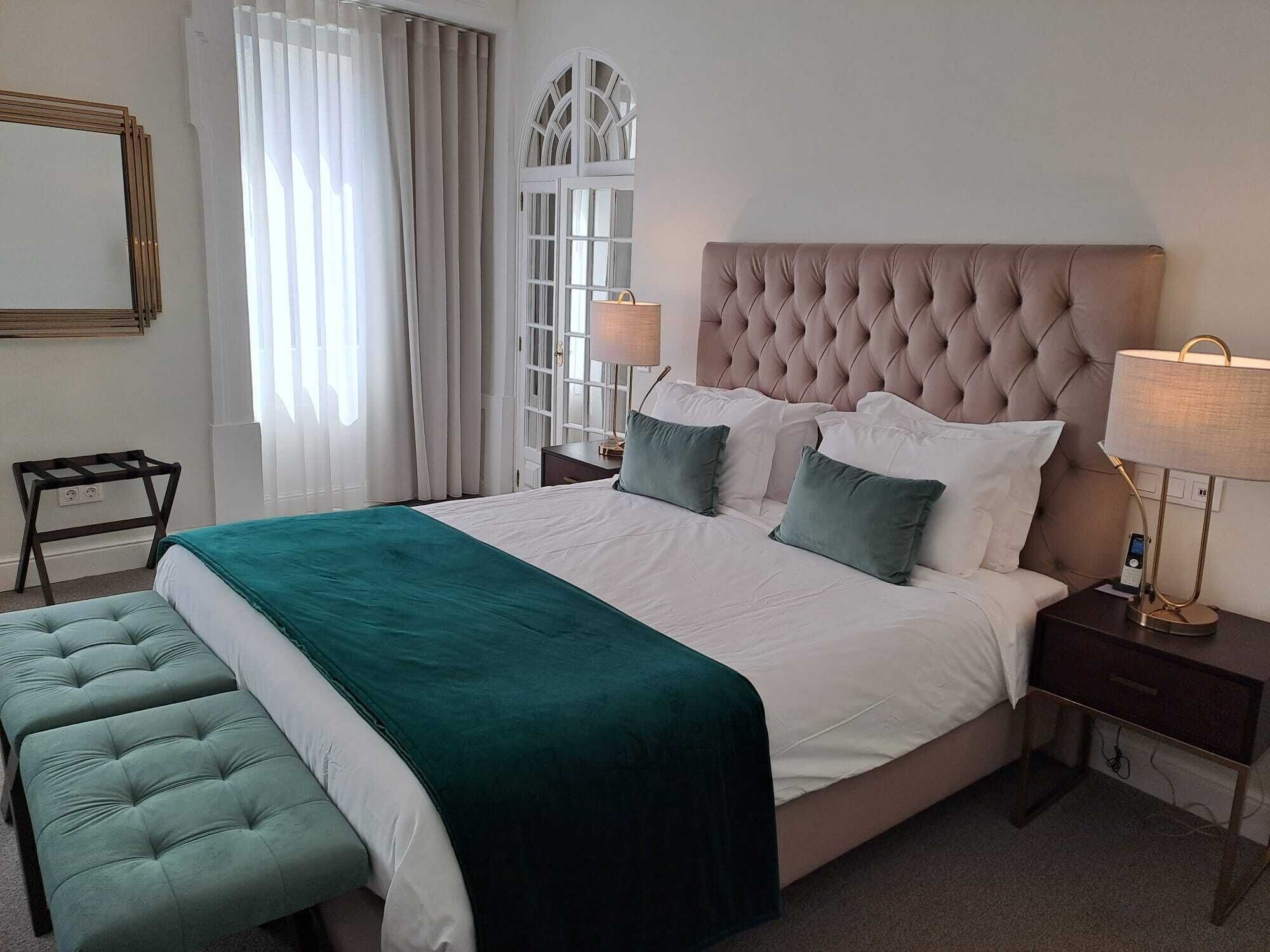 Un dormitorio ordenado con una cama grande, una mesita de noche con lámpara y un banco.