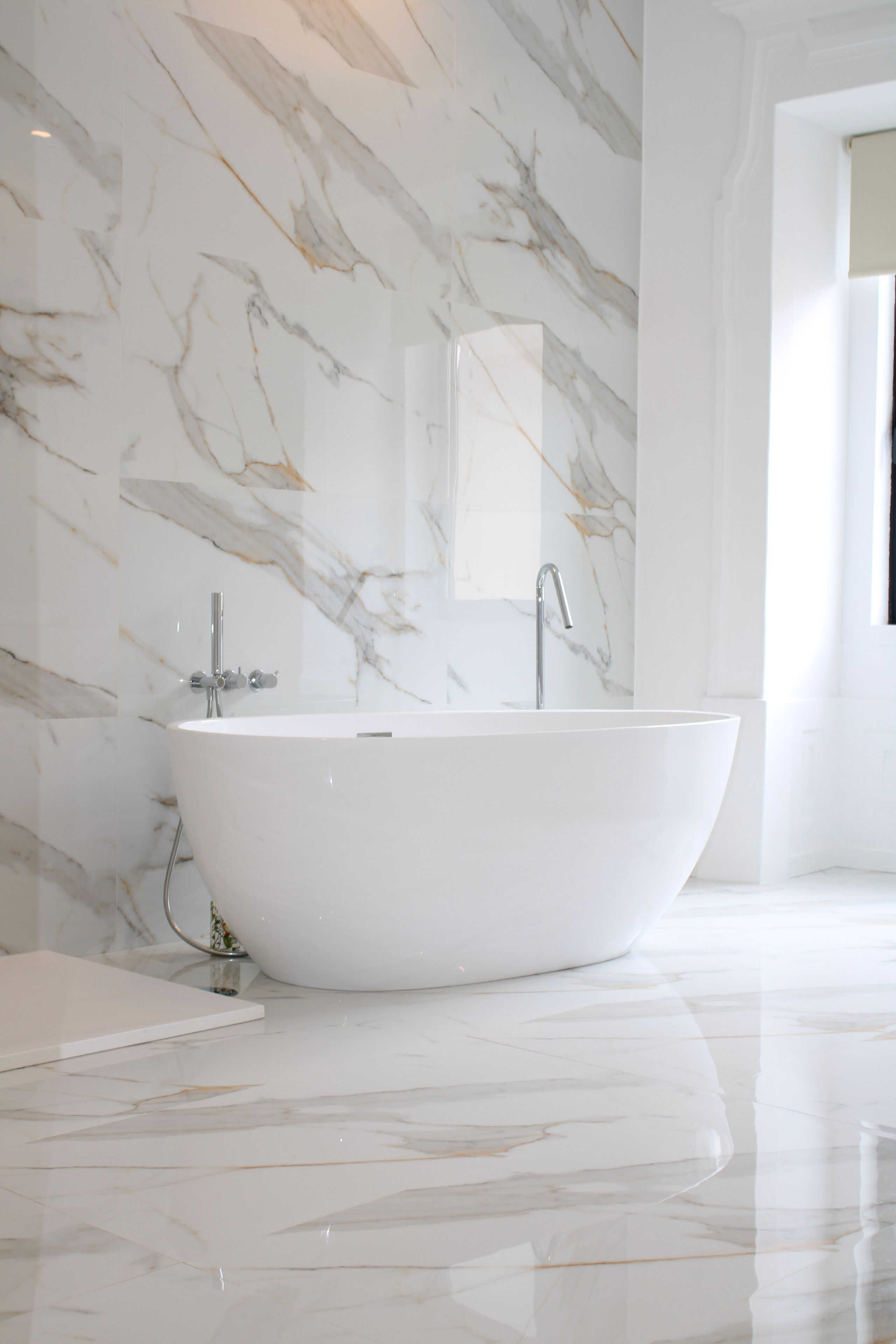 Un bagno moderno con una vasca da bagno indipendente, pareti in marmo e un ampio specchio.