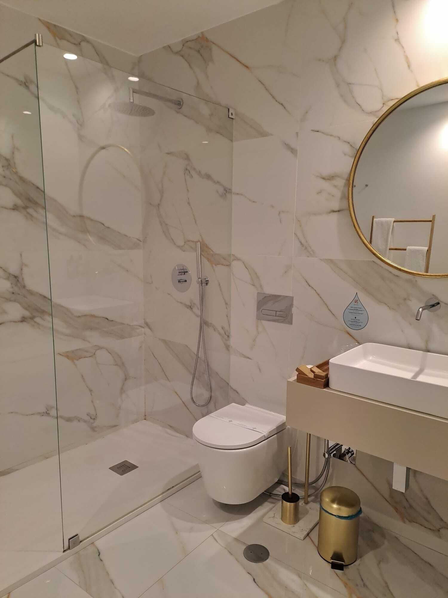 Uma casa de banho moderna com cabine de duche em vidro, sanita branca e toucador com espelho emoldurado a dourado.