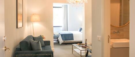 A hotel room with a bed, a desk, a chair, a sofa, a lamp, and a chandelier.
