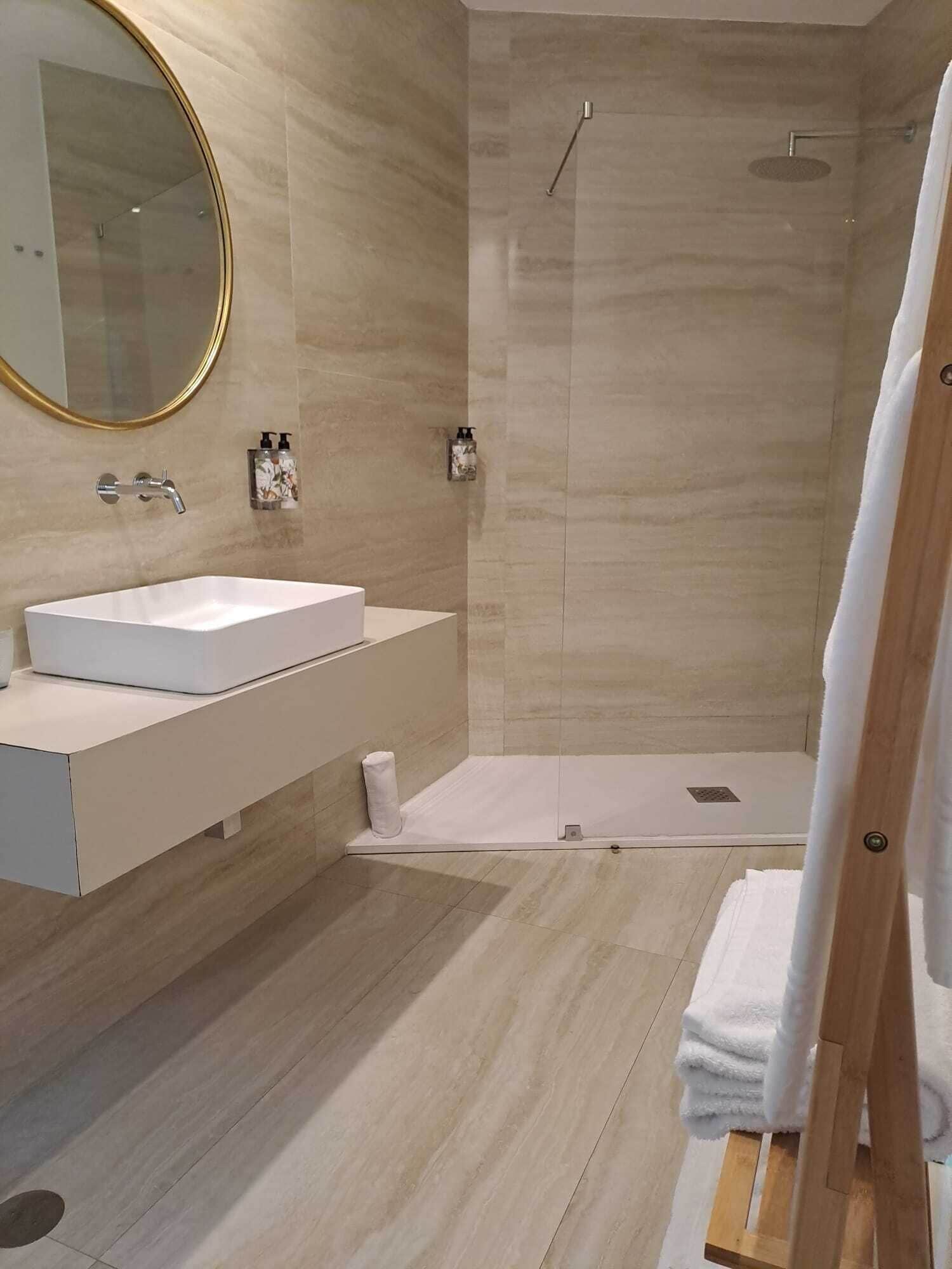 Un baño moderno con un lavabo blanco, un espejo grande y una ducha a ras de suelo.