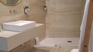Un baño moderno con un lavabo blanco, un espejo grande y una ducha a ras de suelo.