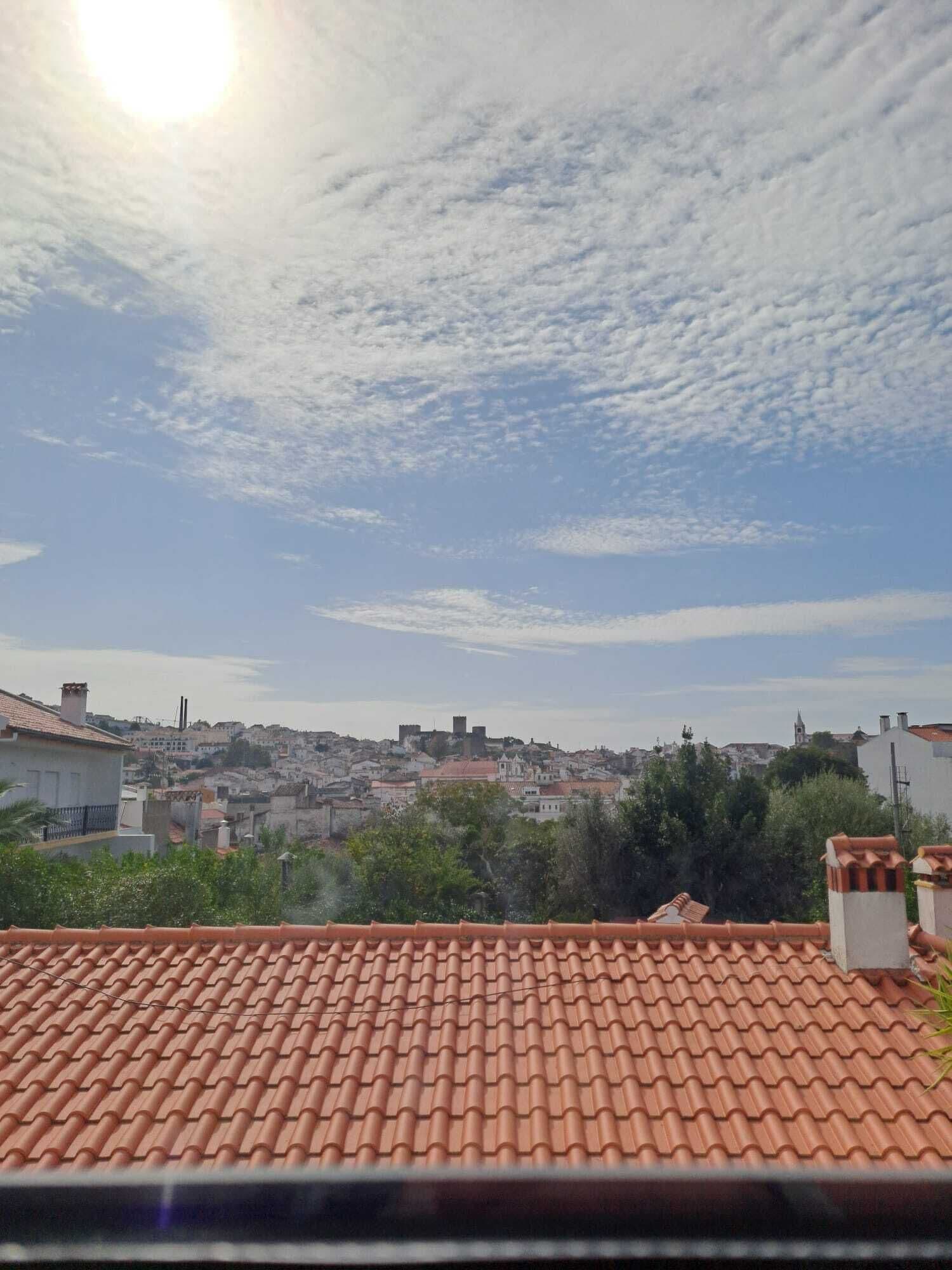 Terrat amb teules de terracota, vista llunyana d'una vila amb edificis històrics, i un cel amb nuvolades disperses.