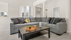 A modern living room with a grey sectional sofa, a dark coffee table, and a wicker side table with a plant. - Between Napa & San Francisco 6bed 4bath Clean (Concord)