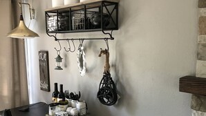 Un comedor con una mesa negra, sillas blancas, una lámpara colgante y un estante de pared con utensilios de cocina.