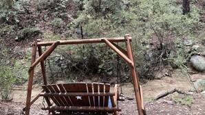 Una mecedora de madera en un área boscosa con un sendero de tierra y rocas.