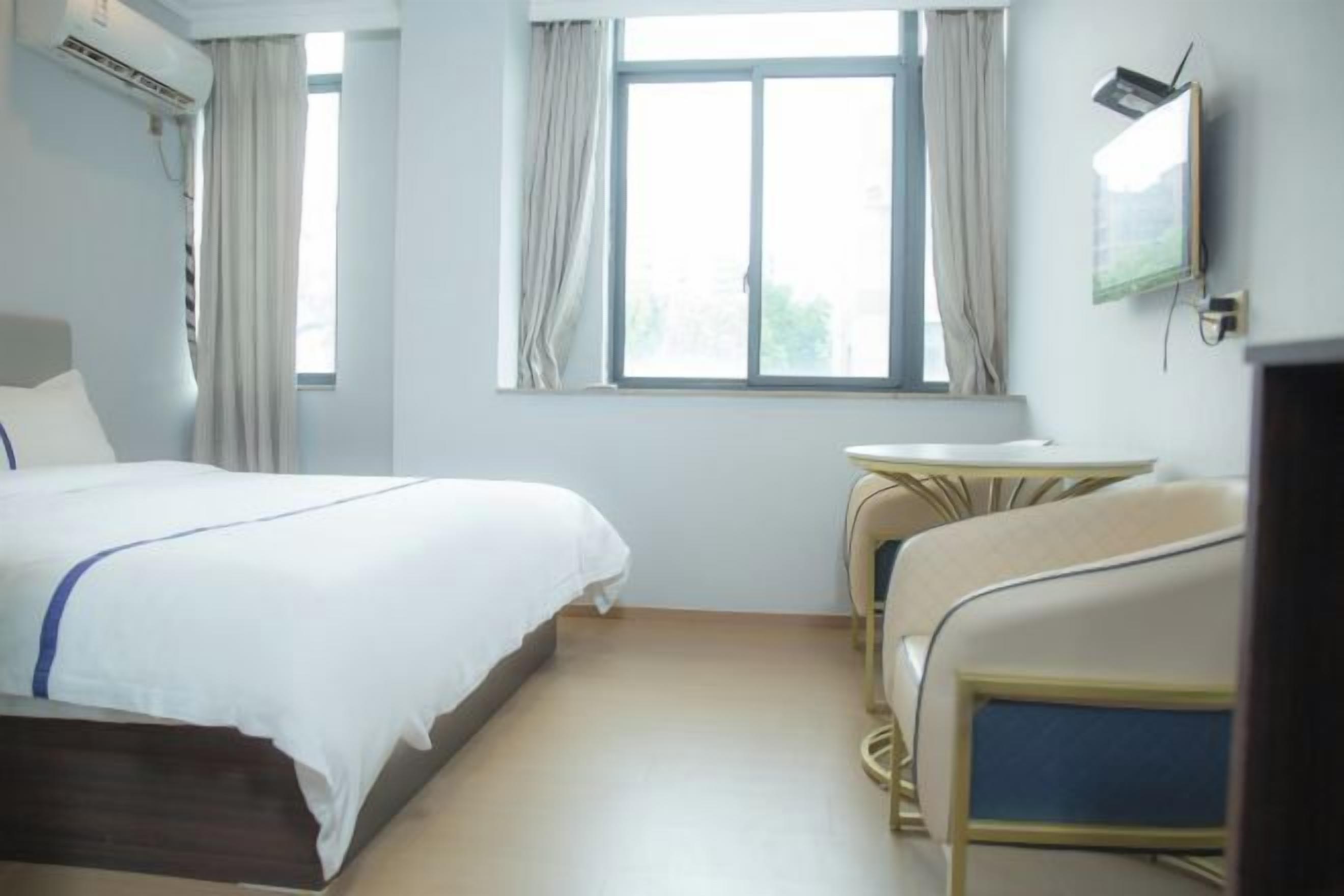 A hotel room with a bed, a small table, a TV, and a window with curtains.