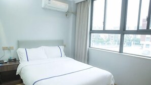 A hotel room with a bed, a nightstand, an air conditioning unit, and a window with curtains. - edinburgh hotel (Haining)