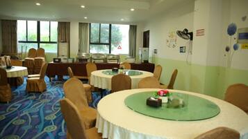 A hotel dining area with multiple round tables, chairs, and a carpeted floor.