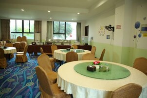 A hotel dining area with multiple round tables, chairs, and a carpeted floor.