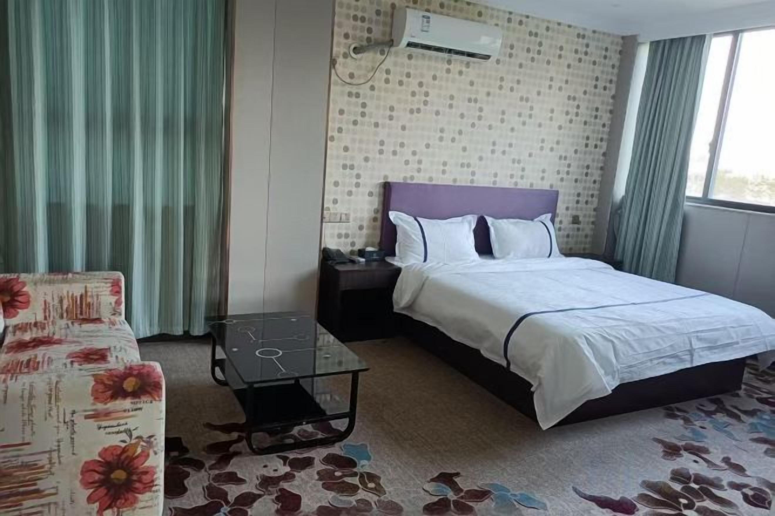 Een hotelkamer met een bed, nachtkastje, stoel, klein tafeltje en een raam met gordijnen.