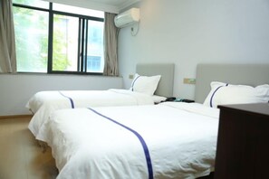 Une chambre d’hôtel avec deux lits, une fenêtre avec des rideaux, un appareil de climatisation et un plancher en bois.