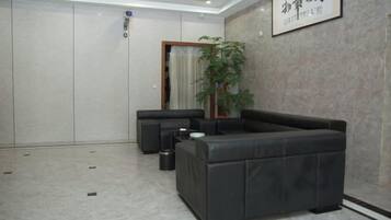 Un hall d’entrée moderne avec un canapé en cuir noir, une plante en pot et un panneau encadré accroché au mur.