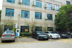 Un estacionamiento con varios autos y un edificio con múltiples ventanas y unidades de aire acondicionado.
