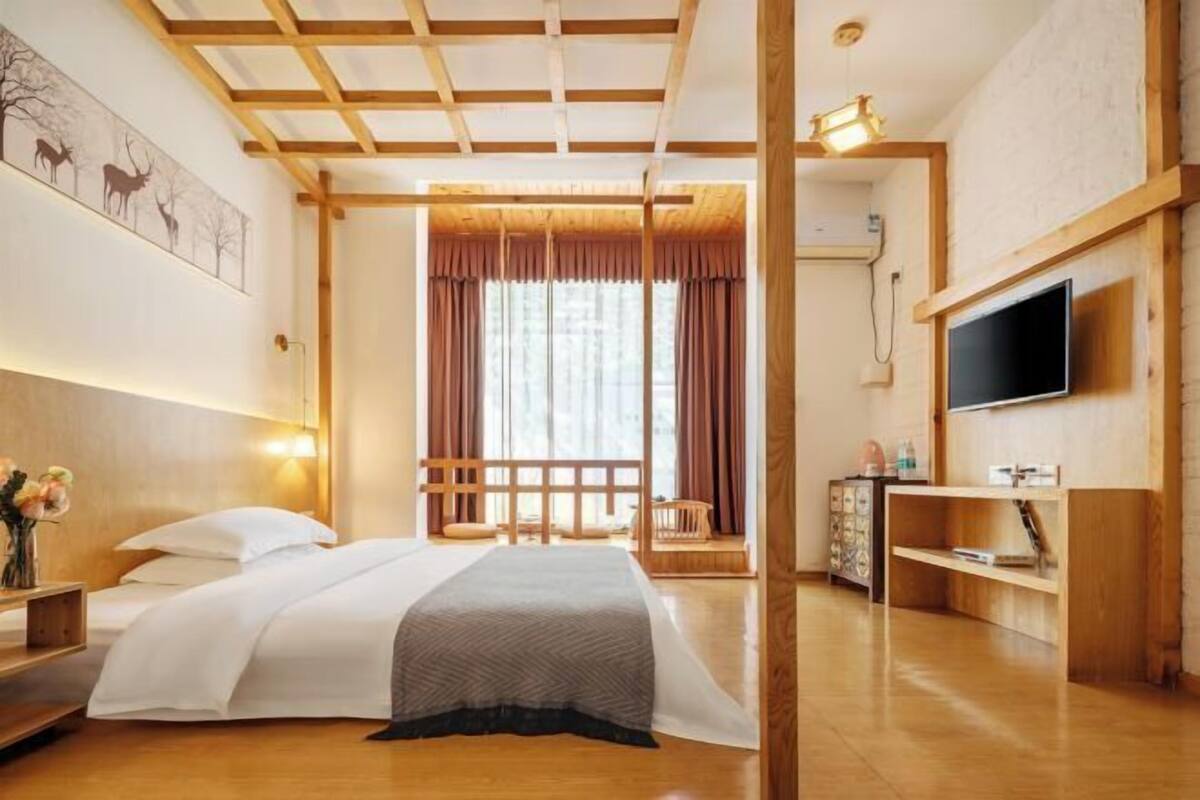 A hotel room with a bed, bedside table, TV, and a large window with curtains.