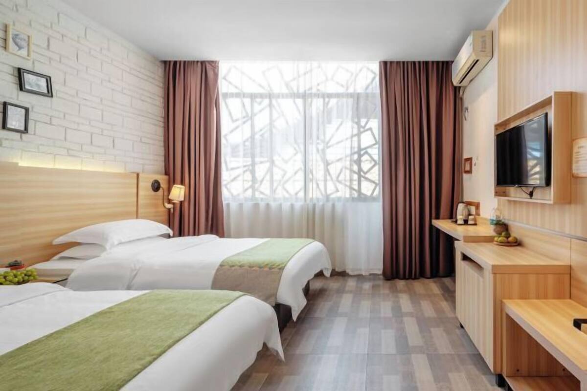 A hotel room with two beds, a wooden desk, a television, and a window with curtains.