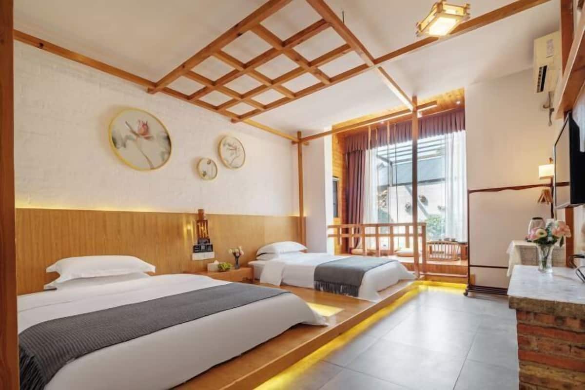 A hotel room with two beds, a wooden ceiling, a small table with a vase, and a window with curtains.