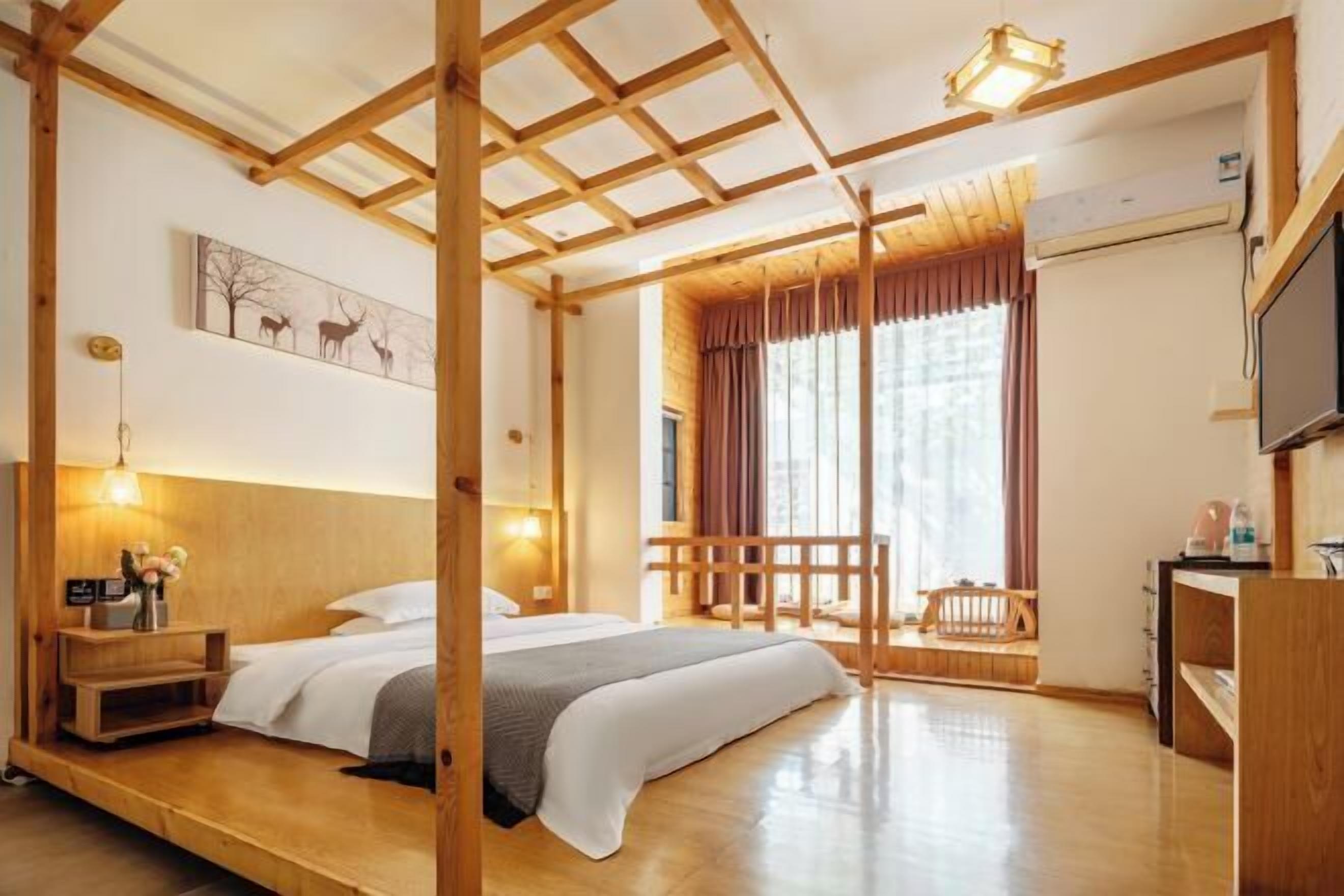 Una habitación con cama, piso de madera, un escritorio, una silla, una ventana con cortinas y un televisor montado en la pared.