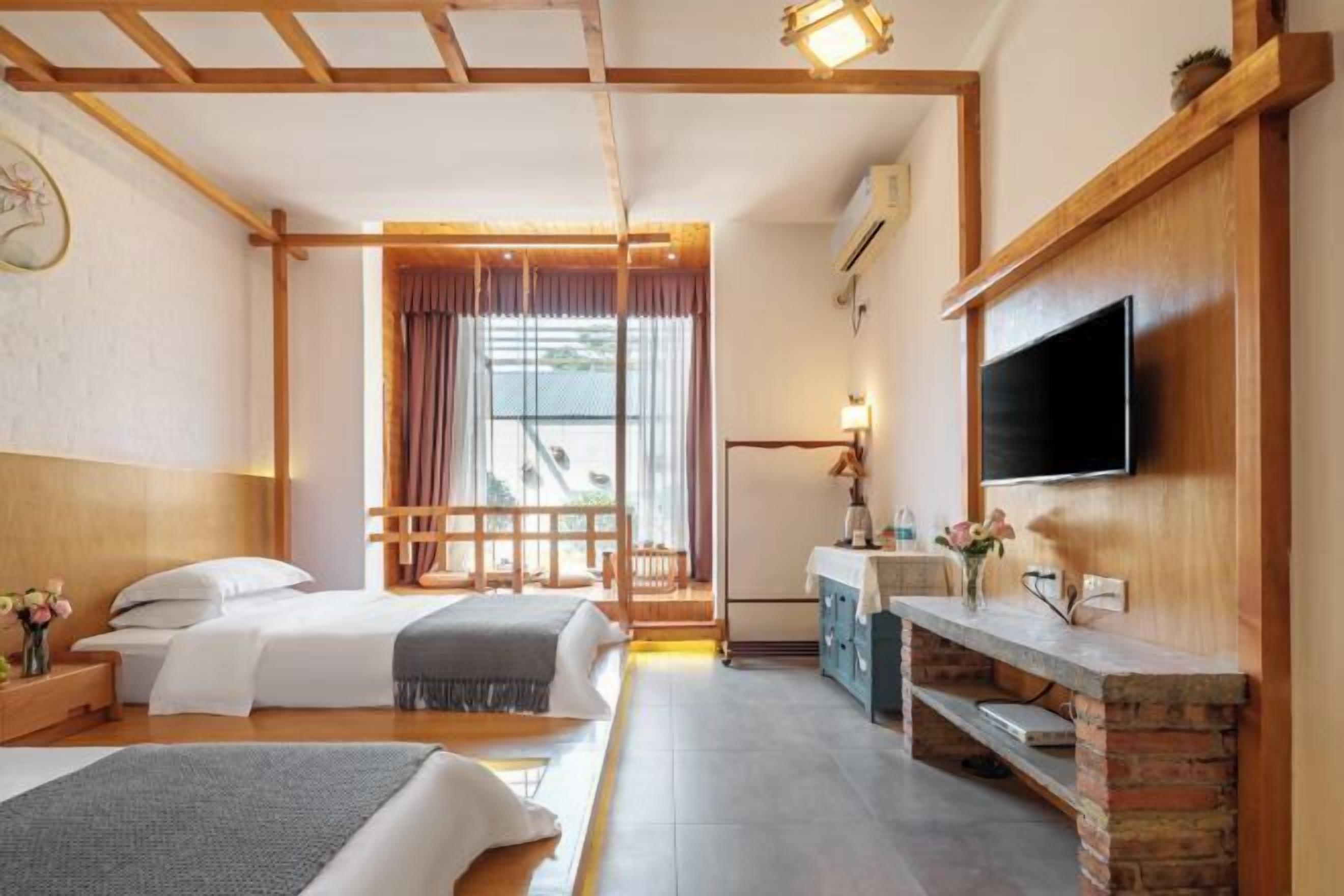 Habitación de hotel con dos camas, televisión, escritorio, ventana con cortinas y techo de madera.