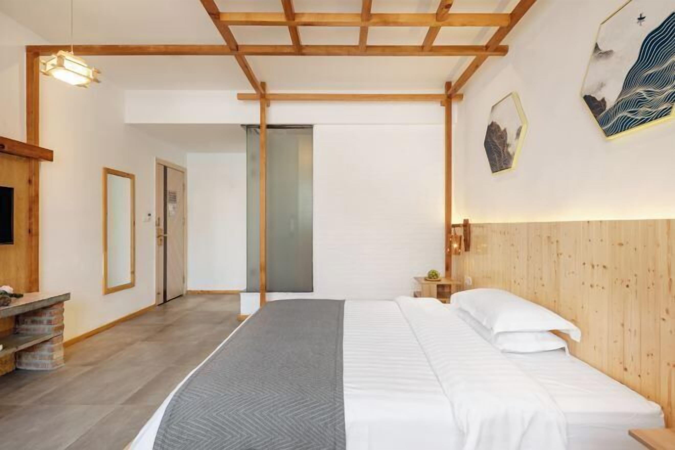 A bedroom with a wooden ceiling, a bed with white bedding, a bedside table, and a wall-mounted light fixture.