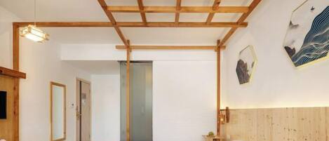 A bedroom with a wooden ceiling, a bed with white bedding, a bedside table, and a wall-mounted light fixture.