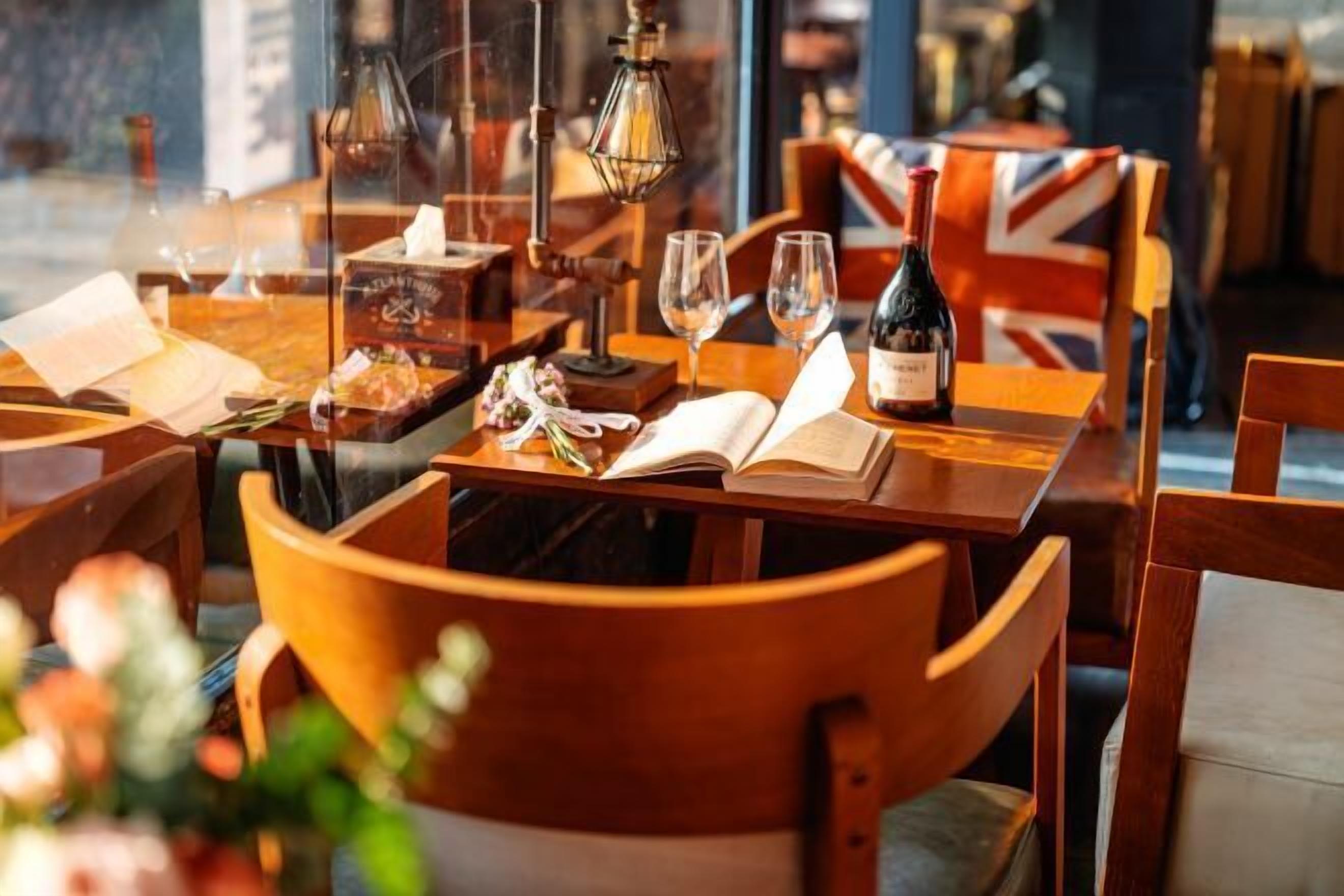 A cozy restaurant setting with wooden tables and chairs, a bottle of wine, glasses, and an open book on the table.