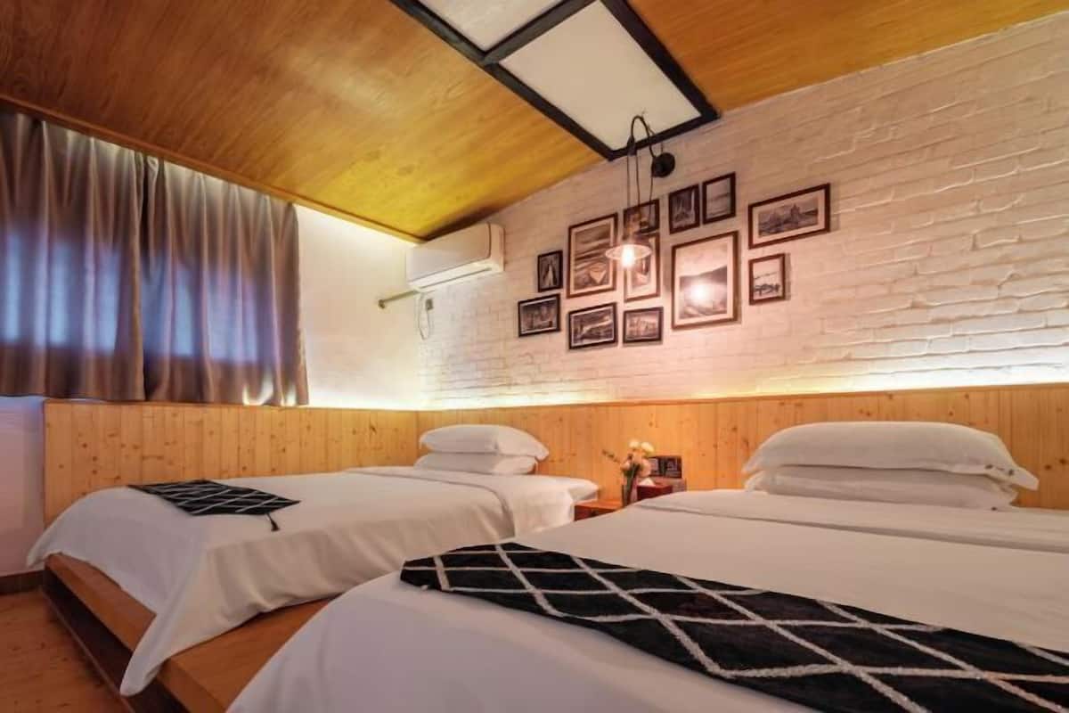 A hotel room with two beds, wooden walls, a sloped ceiling, and framed pictures on the wall.