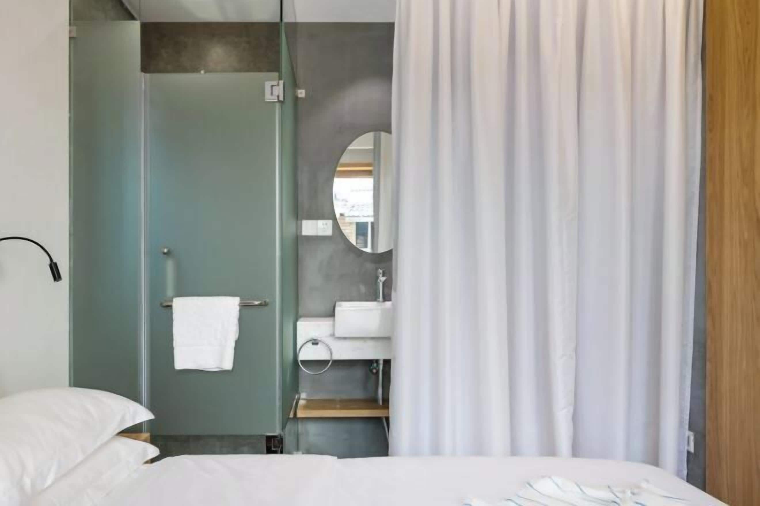 A modern hotel room with a bed, a bathroom with a shower, and a sink.