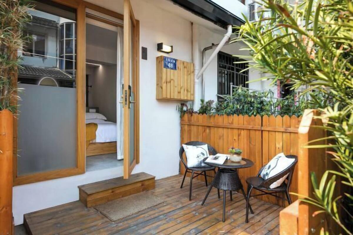 Eine Holzdielen-Terrasse mit einem kleinen Tisch und Stühlen, ein Holzzaun und eine Tür, die zu einem Zimmer mit einem Bett führt.