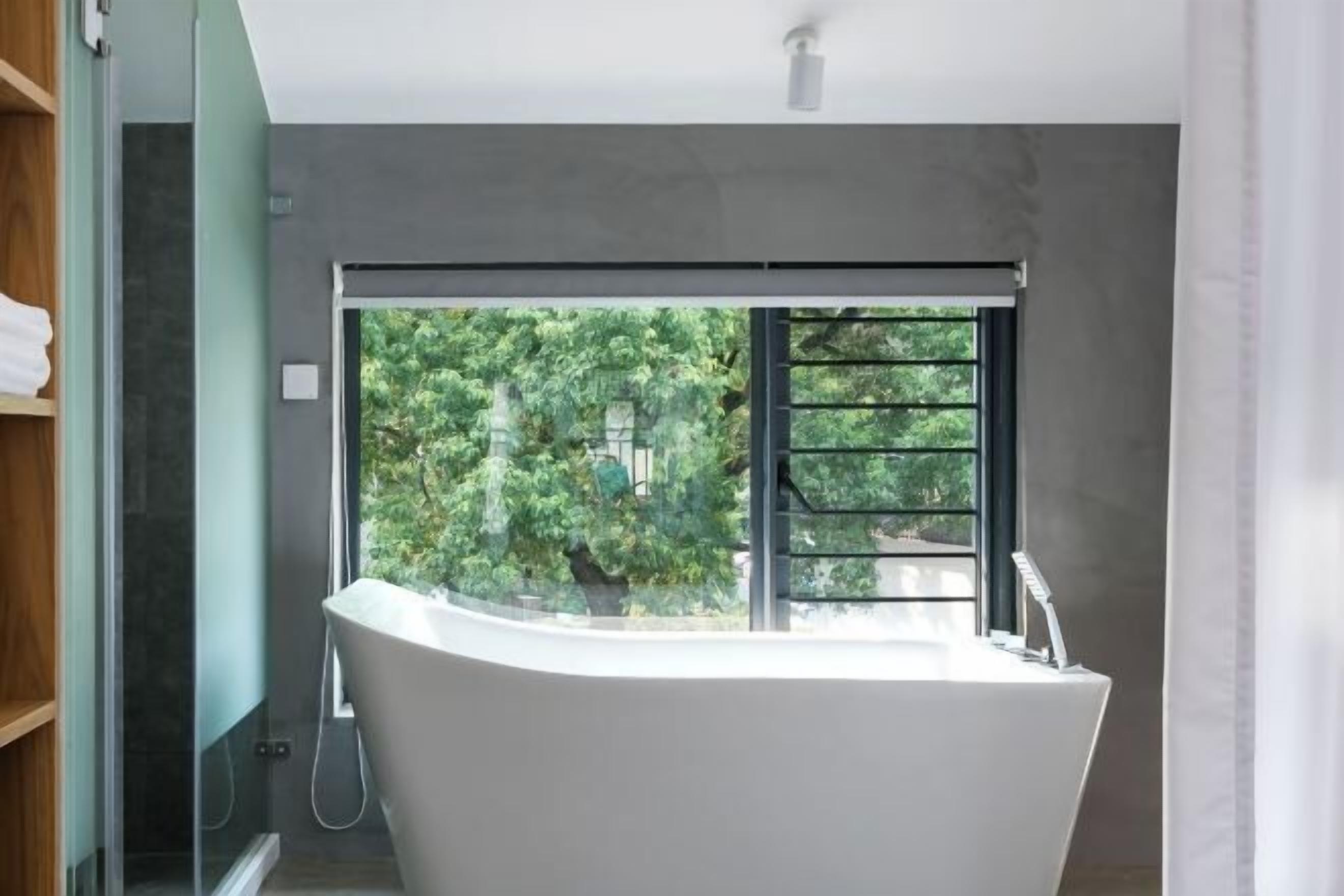 A modern bathroom with a freestanding bathtub, a glass shower enclosure, and a view of greenery outside.